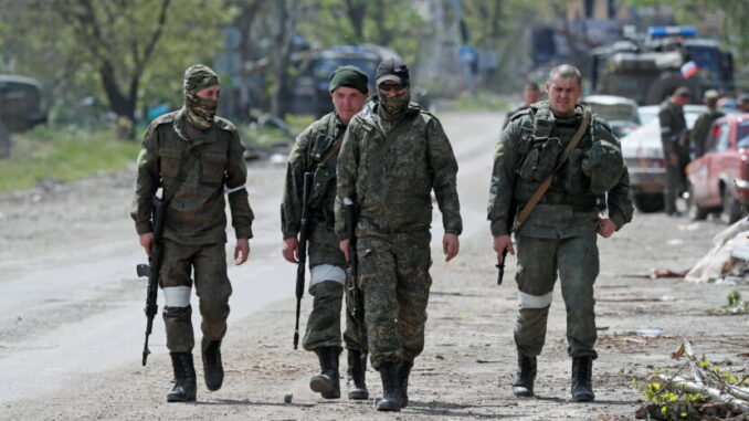Service members of pro-Russian troops walk along a street in Mariupol