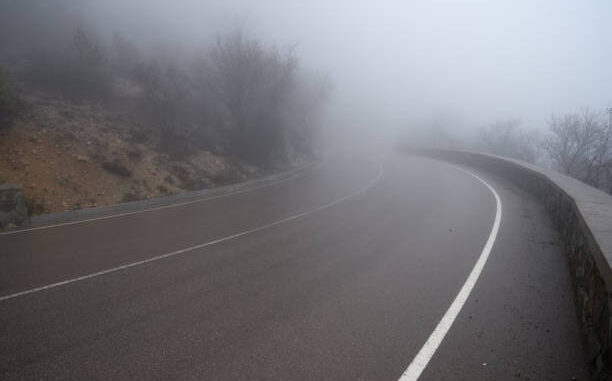 A curved asphalt road with white road markings going into the fog.